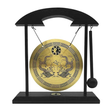 A black desktop stand holding a round brass gong with intricate carvings and a wooden mallet.