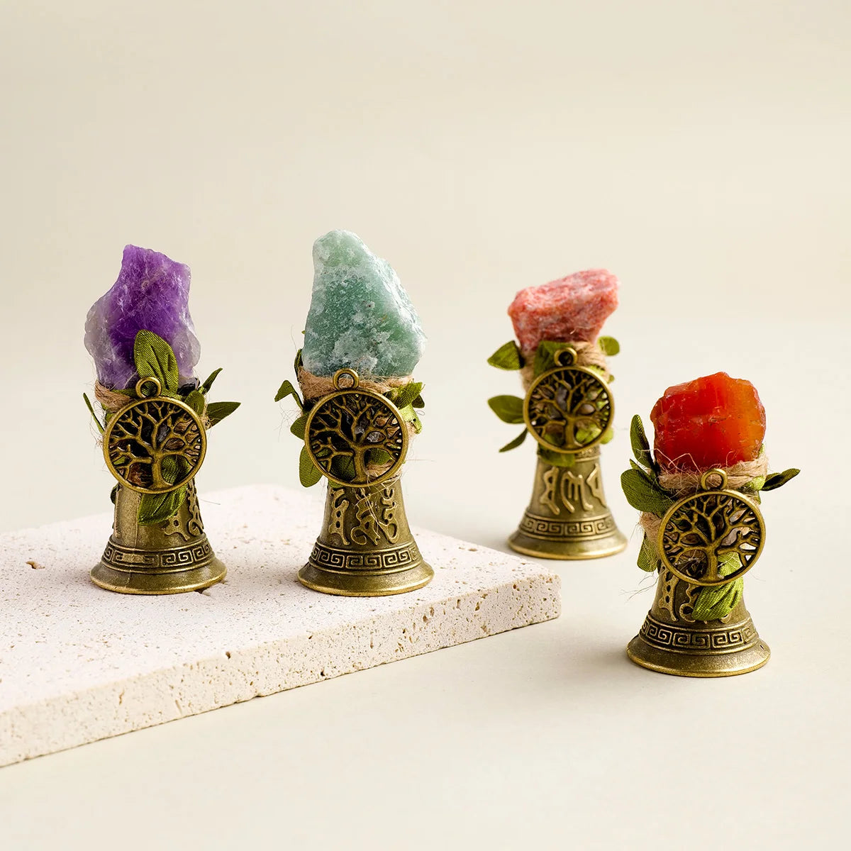Three natural crystal specimens are displayed in brass bells with copper finish and green foliage.