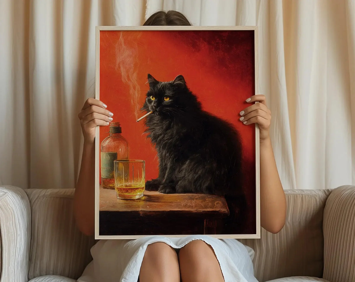 A person holds a framed poster featuring a black cat smoking on a wooden surface against a red background.