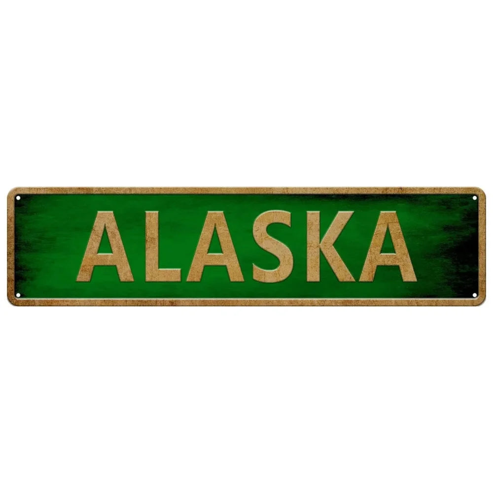 A rectangular green metal tin sign with the word ALASKA written in gold lettering.