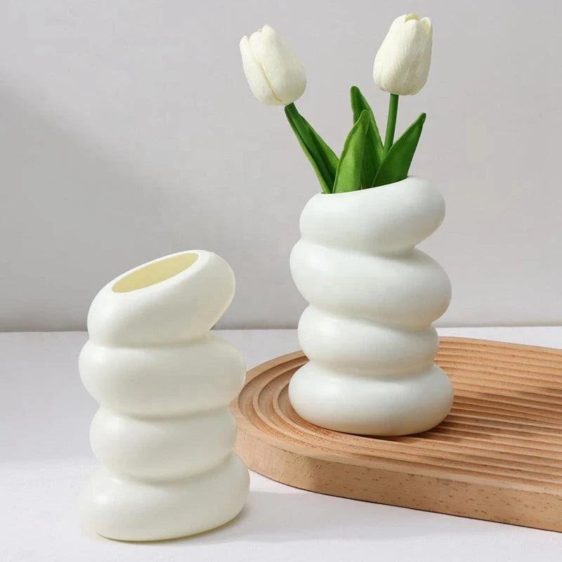 A white ceramic vase with a spiral design holds a single white tulip flower on a wooden surface.