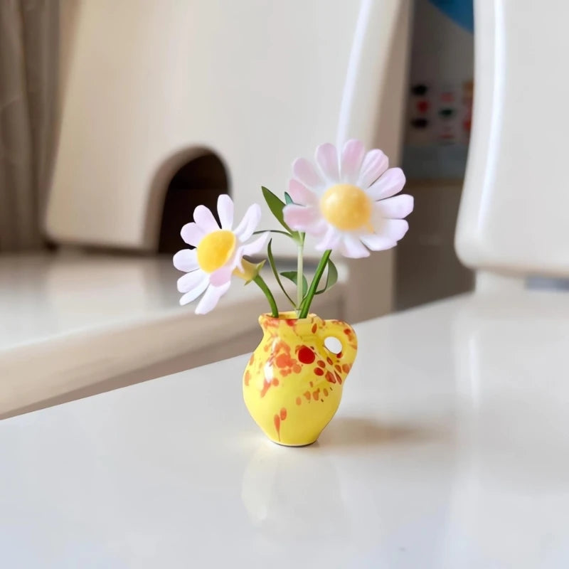 A yellow ceramic vase holding three pink and white daisy-like flowers on a white surface.