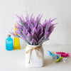 A bouquet of purple lavender flowers in a white vase on a white surface.