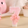 A single pink glitter birthday candle shaped like the number 7 with a pink bow on a white base.