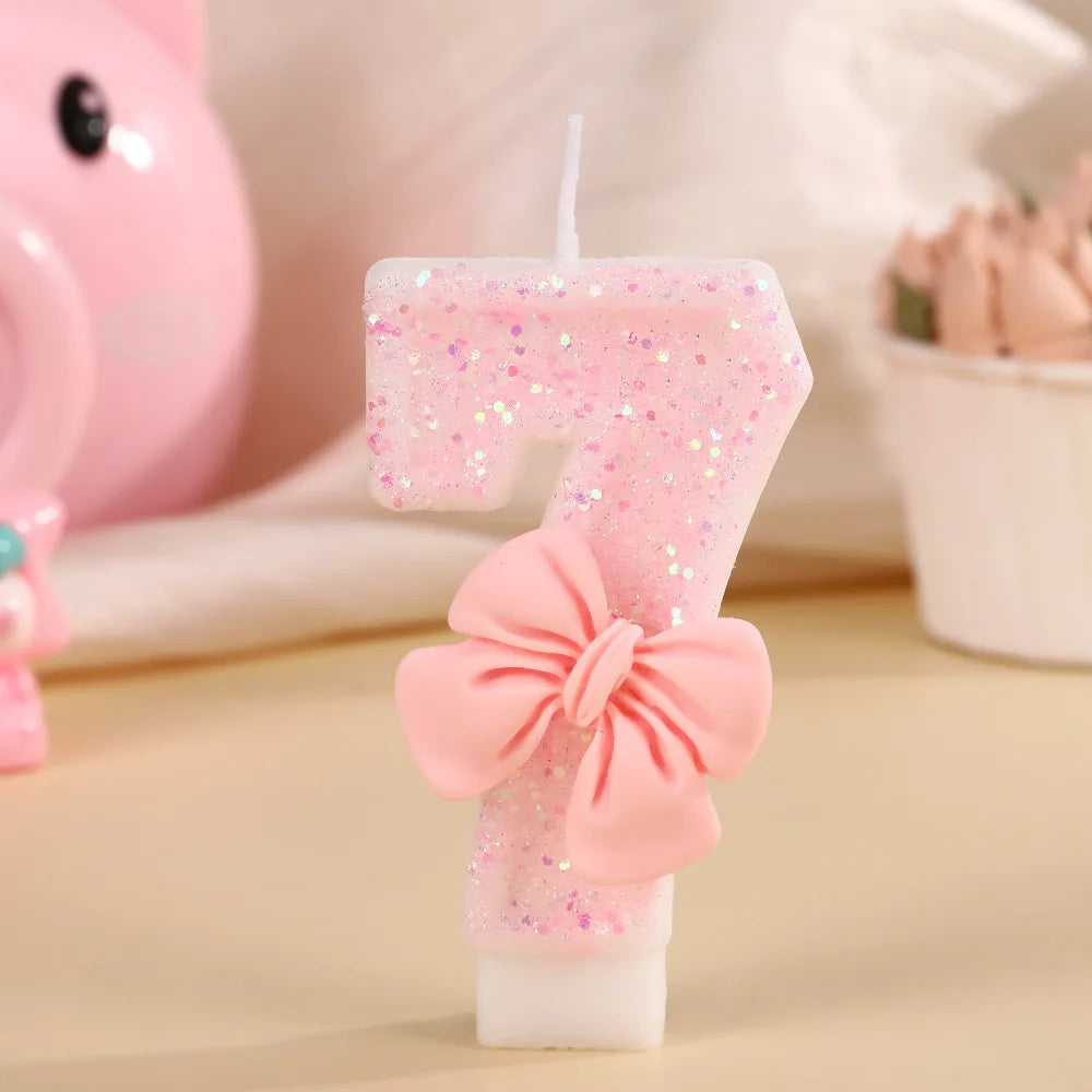 A single pink glitter birthday candle shaped like the number 7 with a pink bow on a white base.