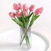 A bouquet of pink artificial tulips in a clear glass vase on a white plate.