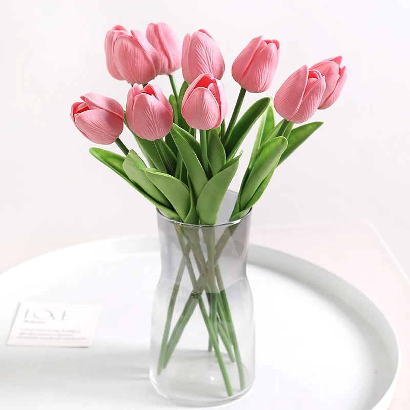 A bouquet of pink artificial tulips in a clear glass vase on a white plate.