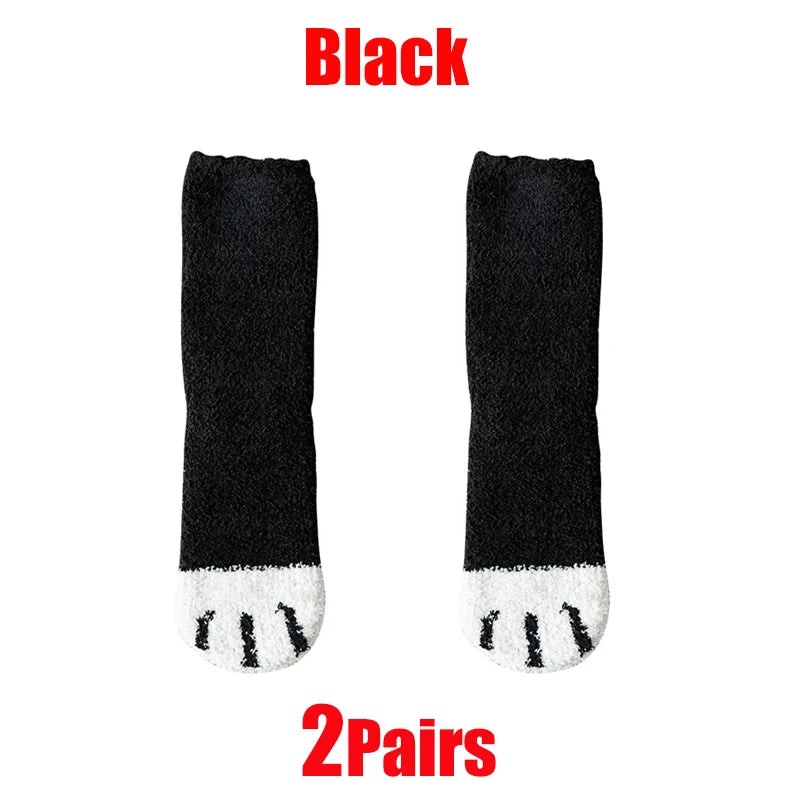 A pair of black plush socks with white cat paw prints on the toe, shown against a white background.