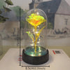 A glass dome containing a golden rose with an internal LED light, displayed on a white surface.