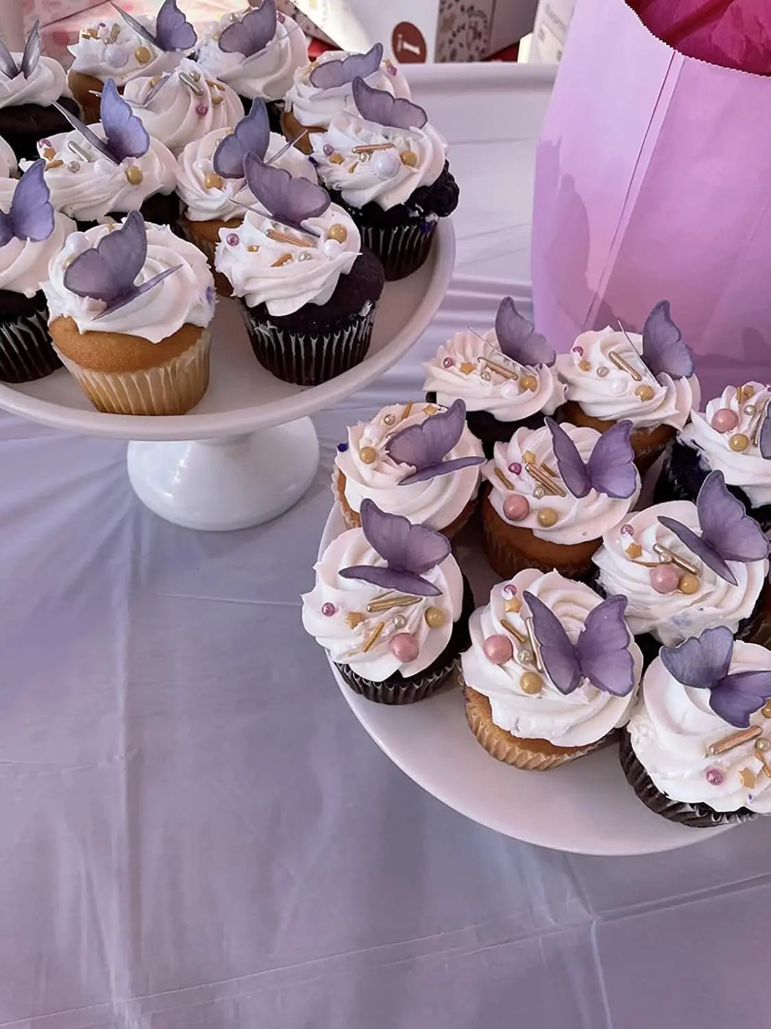 A platter of cupcakes decorated with white frosting and purple butterfly toppers on a white table.