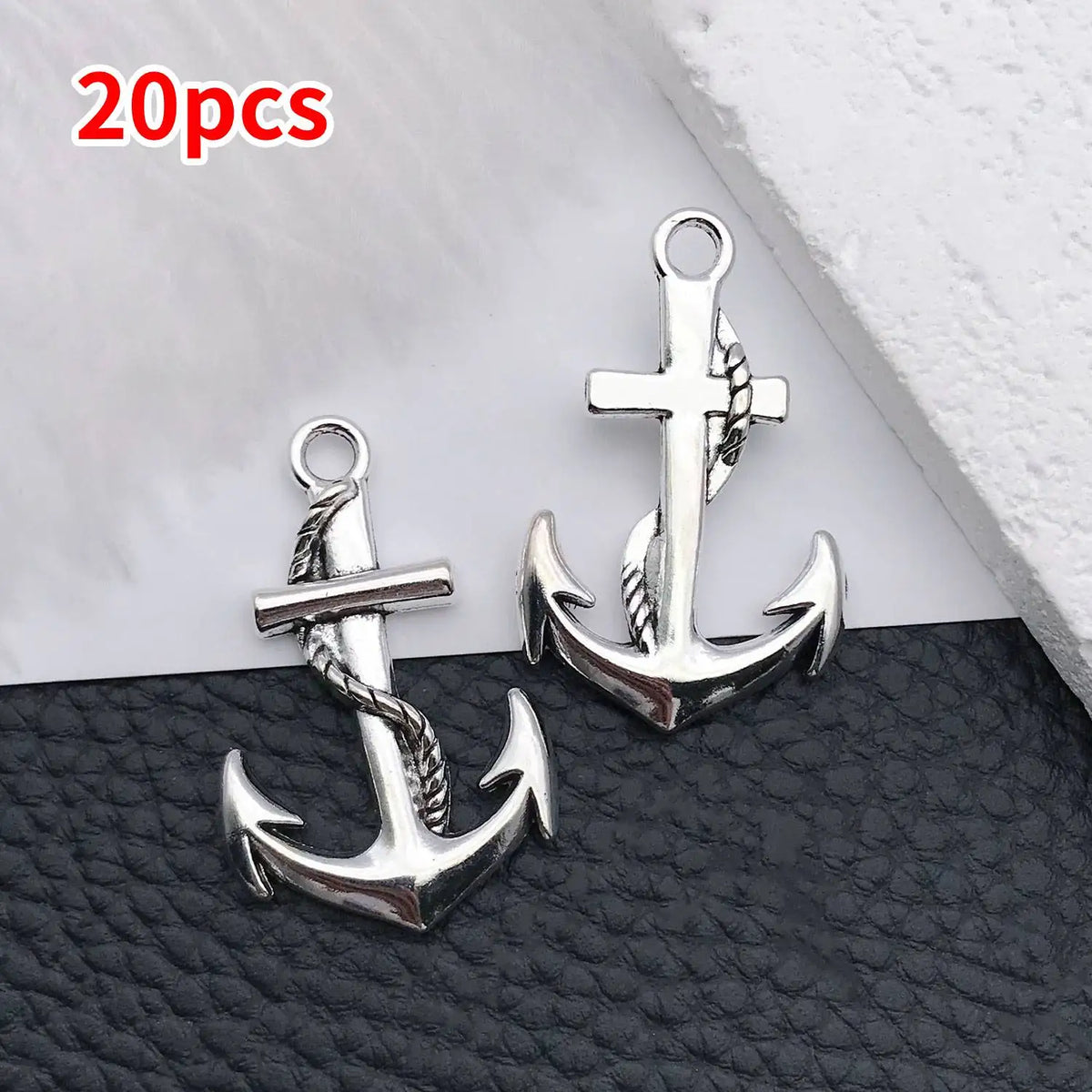 A pair of silver vintage ship anchor charms with braided ropes displayed on a dark surface.