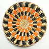 Round woven straw wall decor hanging featuring black and bright orange geometric patterns