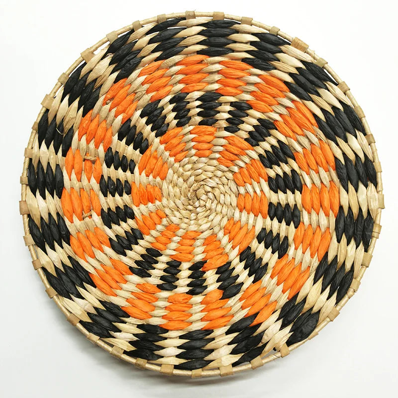 Round woven straw wall decor hanging featuring black and bright orange geometric patterns