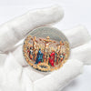 A silver commemorative coin depicting scenes from the Crucifixion and Resurrection, held in a gloved hand.
