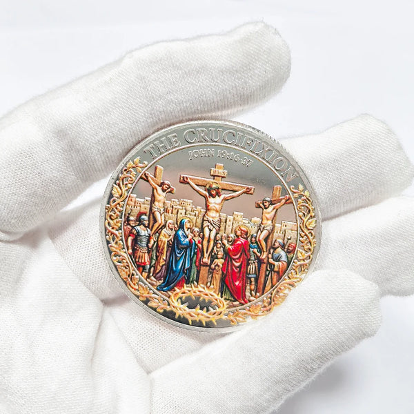 A silver commemorative coin depicting scenes from the Crucifixion and Resurrection, held in a gloved hand.