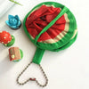 A green foldable hand fan with a red fruit design, next to a blue flower and a red and green ladybug.