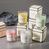 A collection of scented candles in glass jars and boxes, featuring yellow, green, and pink scents.