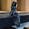 A black figurine of a woman in a hooded gown sitting on a dark surface.