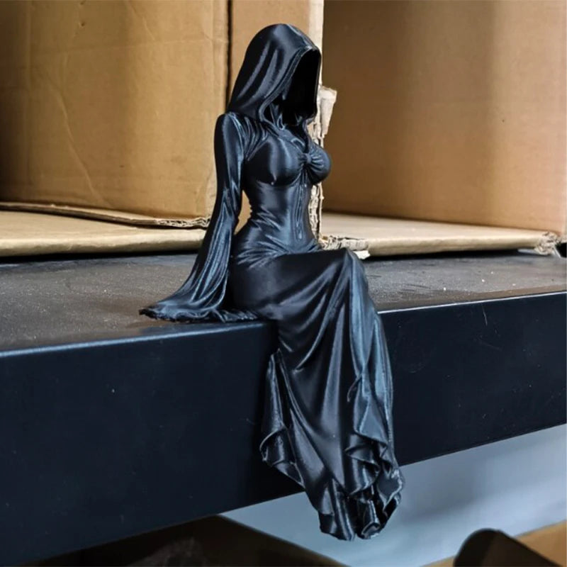 A black figurine of a woman in a hooded gown sitting on a dark surface.