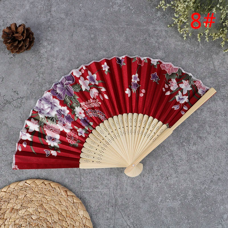 A red and purple floral hand carved bamboo folding fan displayed on a gray surface.