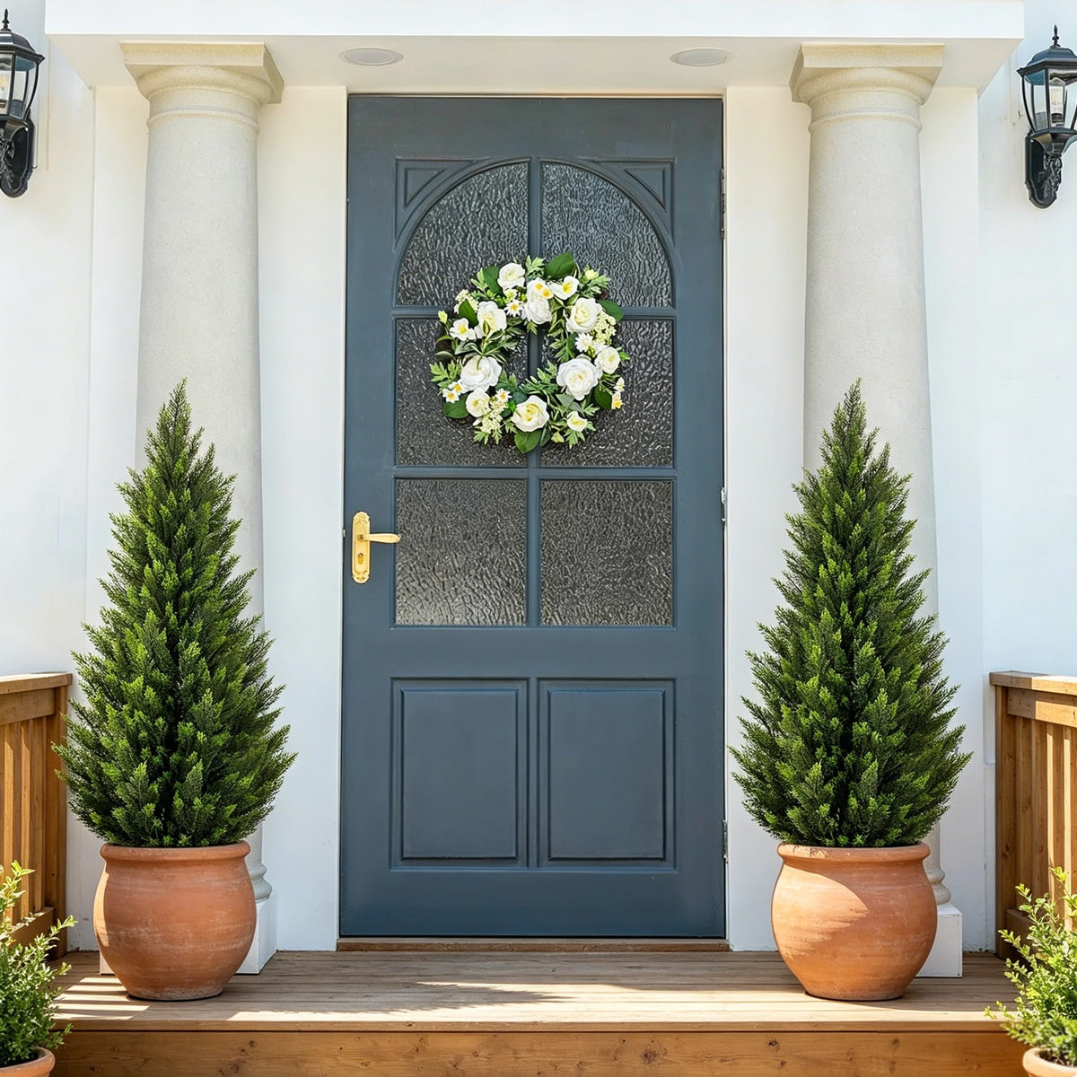 A dark gray door with glass panels flanked by tall white columns and potted evergreen trees.