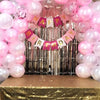 A backdrop of pink and white latex balloons with confetti banners for a birthday celebration