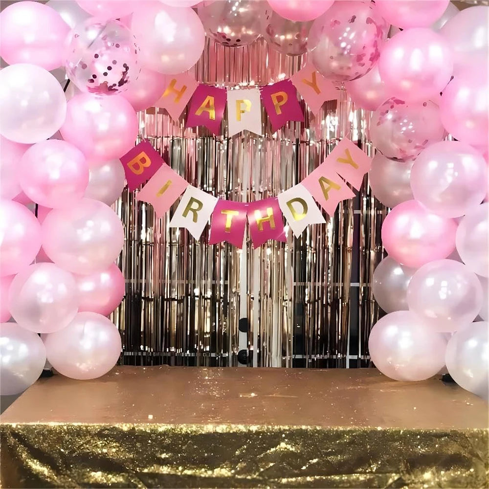 A backdrop of pink and white latex balloons with confetti banners for a birthday celebration