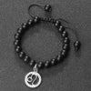 A black beaded bracelet with a silver zodiac charm is displayed on a dark surface.