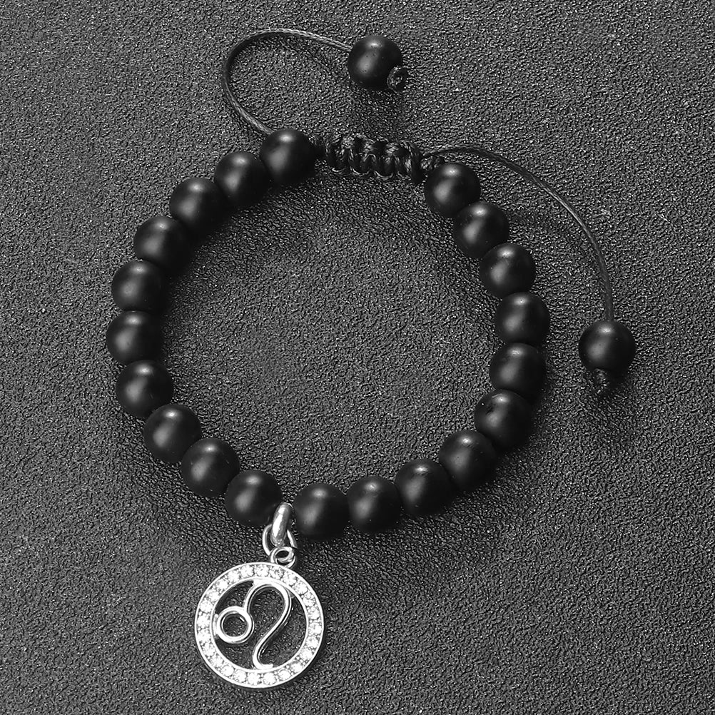 A black beaded bracelet with a silver zodiac charm is displayed on a dark surface.