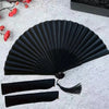 A black folding hand fan with a bamboo frame is displayed on a white surface.
