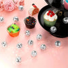 A collection of ten silver disco ball ornaments and various decorated cupcakes are arranged on a pink surface.