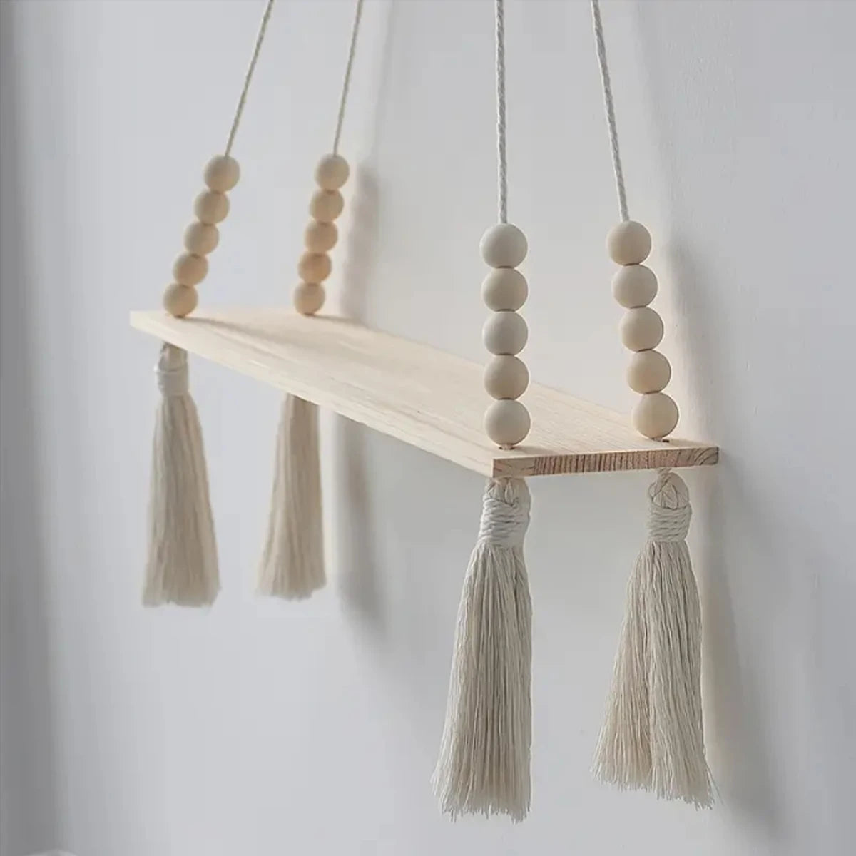 Handmade macrame wood wall shelf with tassels hanging on a white wall.
