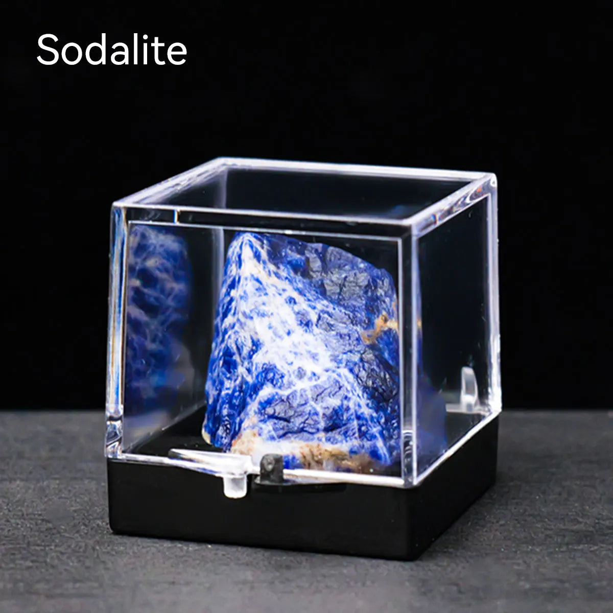A clear glass box displaying a rough blue and white crystal specimen on a black base.