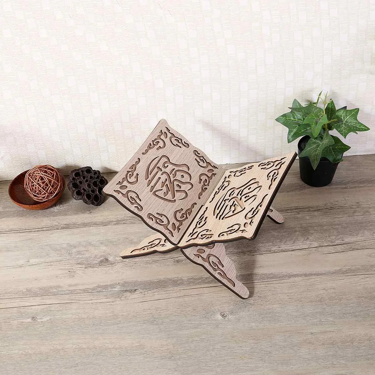 Handcrafted wooden Quran book stand with intricate Arabesque design resting on a wooden surface next to a potted plant.