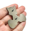 A hand holds a set of silver-colored enamel pins shaped like a cat for jackets and backpacks.