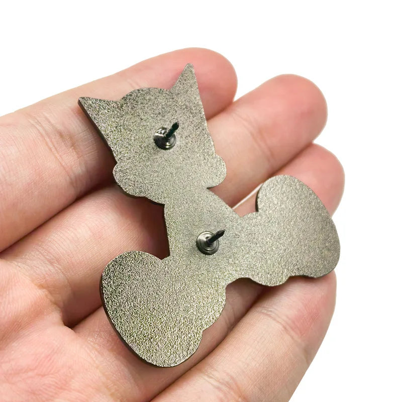 A hand holds a set of silver-colored enamel pins shaped like a cat for jackets and backpacks.