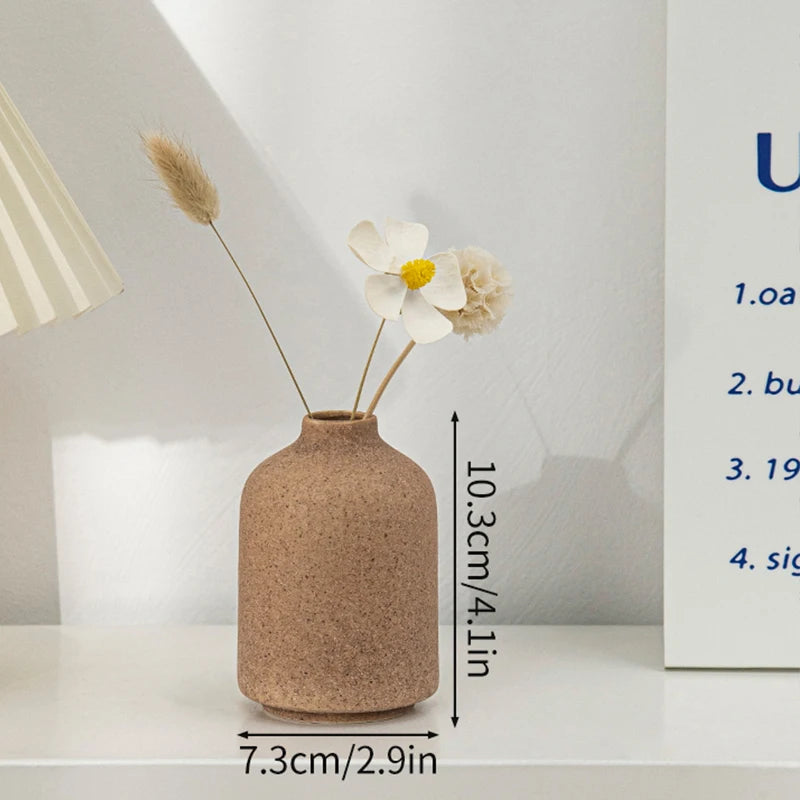 A minimalist ceramic vase in a beige tone holds dried floral elements on a white surface.