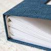 A dark blue linen cover photo album with a sleeve open, displaying multiple white pockets.