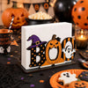 A wooden tissue dispenser shaped like a Boo pumpkin with black and white ghost patterns.