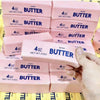 Pink butter squeeze toys in various sizes and packaging are shown being held by a hand.