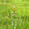 A gold flame moon crystal sun catcher with a central eye design and dangling crystals suspended against a green background.