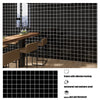 A black grid pattern self-adhesive backsplash panel installed on a wooden countertop in a modern kitchen setting.