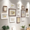 A collection of thirteen wooden picture frames in various sizes and tones displayed on a light gray wall.
