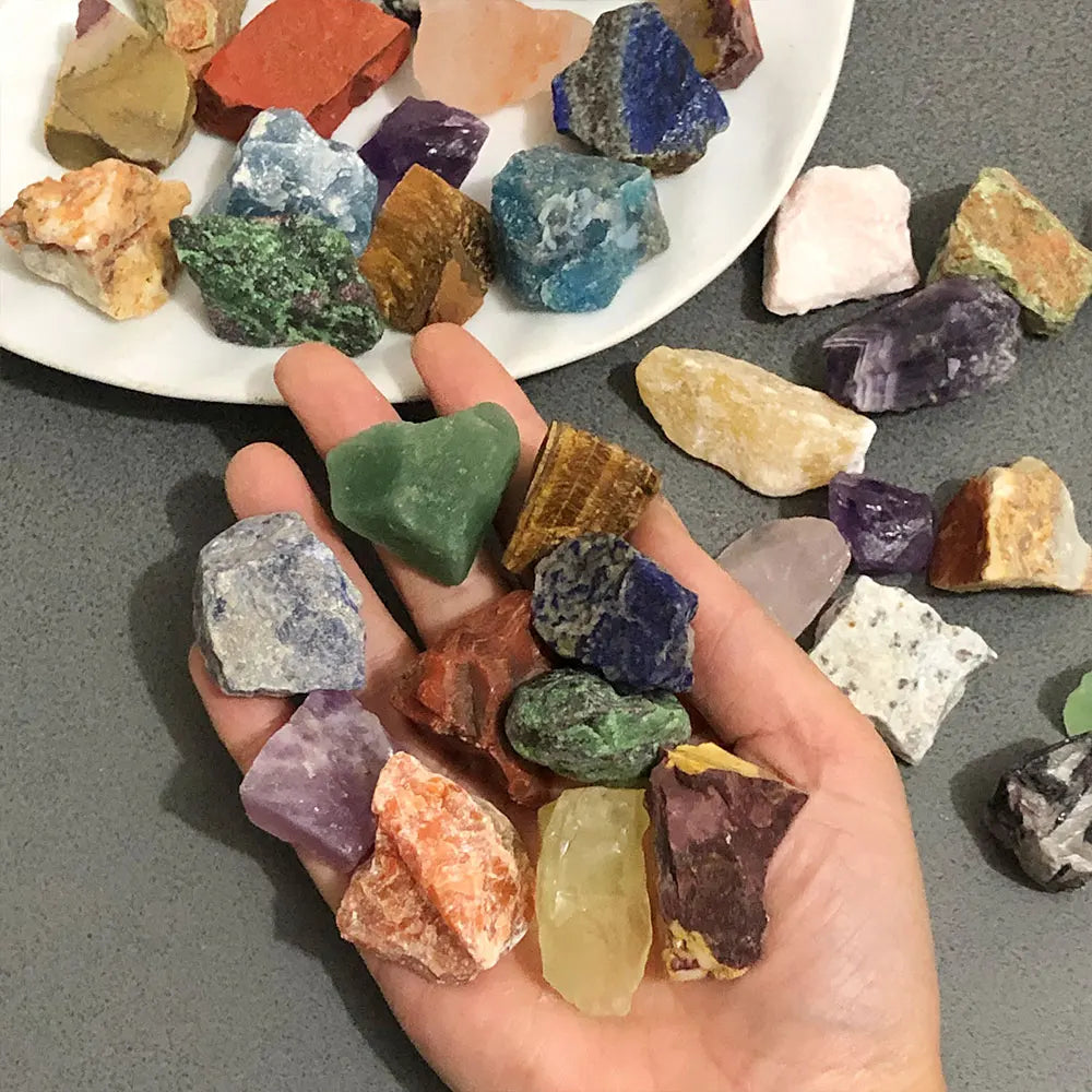 A hand holds a collection of assorted natural raw crystal stones and healing minerals in various colors and shapes.