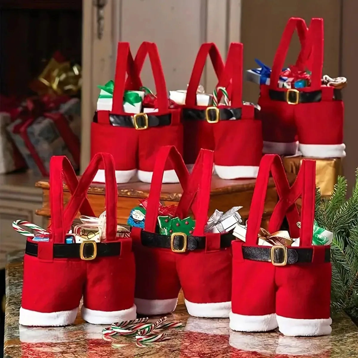 A set of six festive red Santa Claus gift bags with black belts and white trim displayed on a wooden surface.