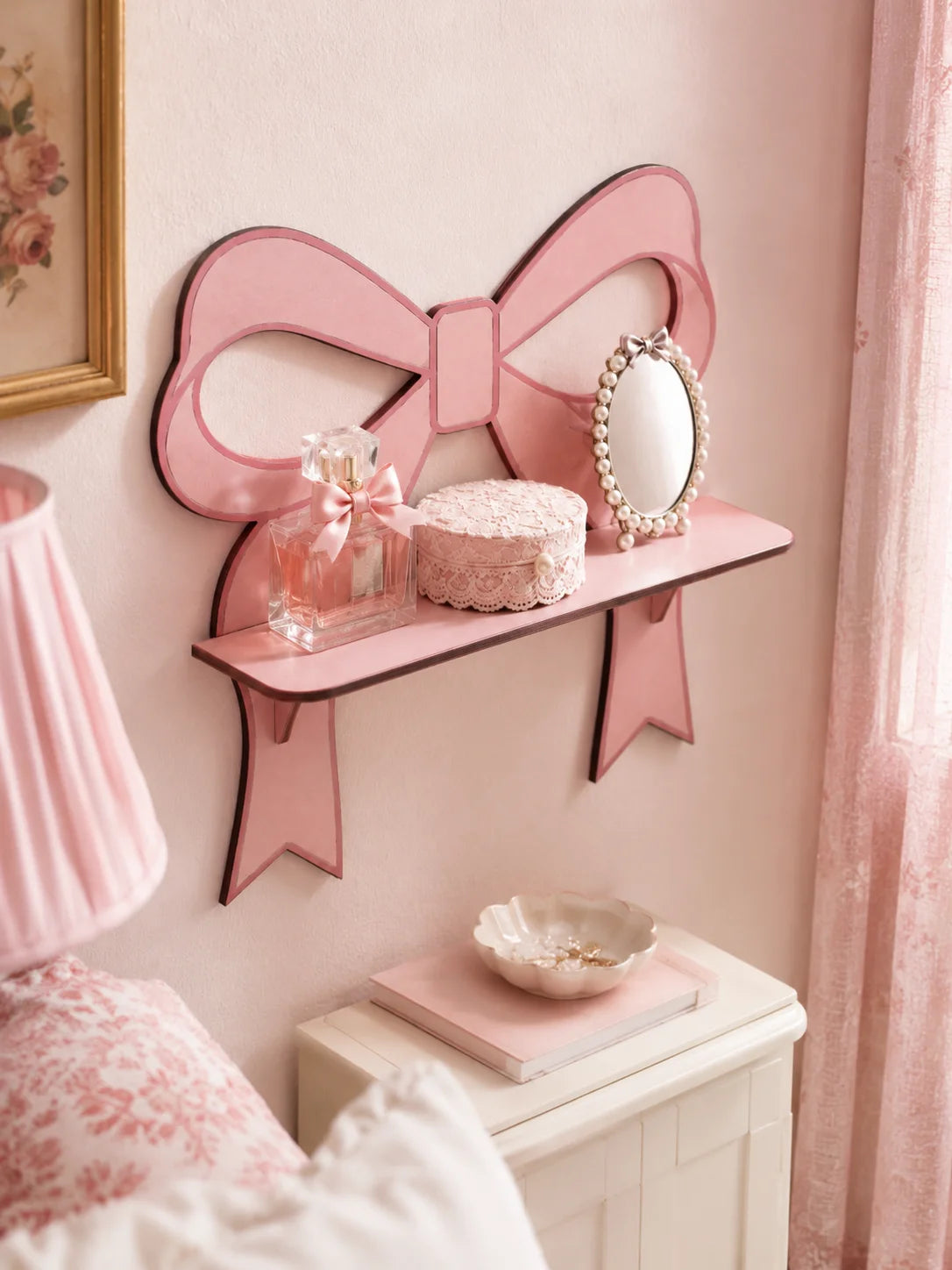 A pink wooden wall shelf shaped like a bow holds a mirror and a glass jar on a light pink wall.