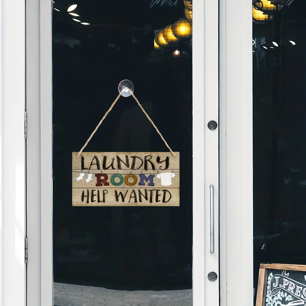 A vintage wooden farmhouse hanging sign with a leather cord and wooden plaque that reads Laundry Room Help Wanted