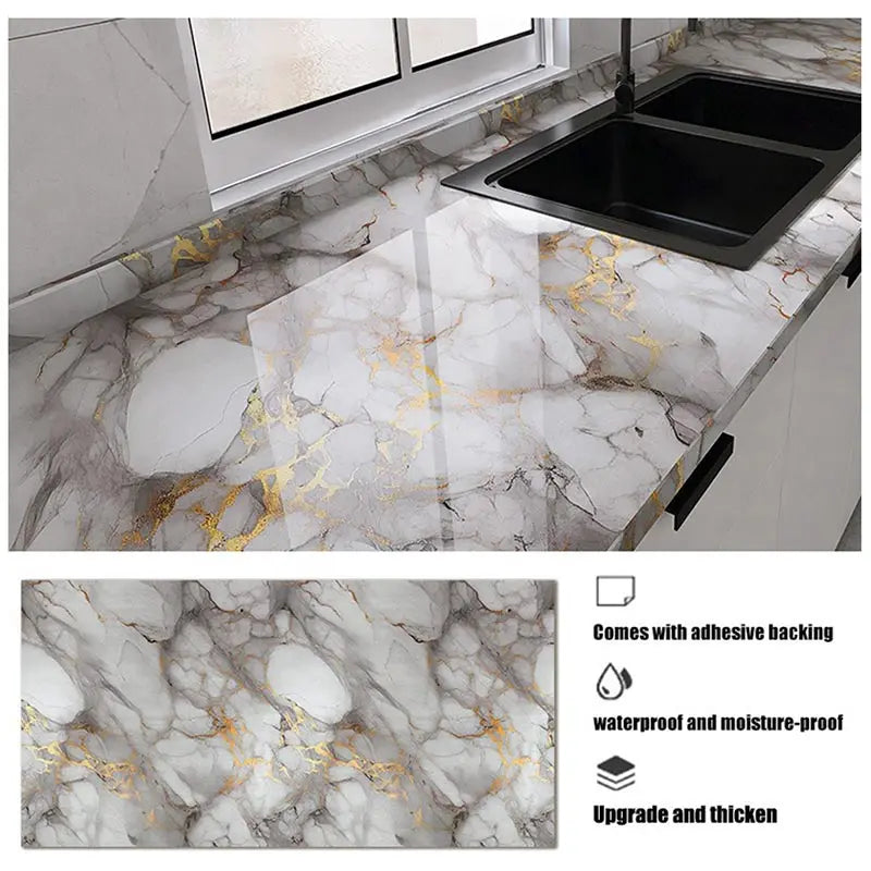 A black kitchen sink installed on a marble countertop featuring gold leaf veining and adhesive backing.