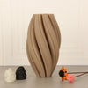 A textured wave vase in soft morandi tones sits on a surface next to small decorative objects.