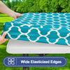 A teal waterproof elastic fitted tablecloth is being held over a white table surface outdoors.